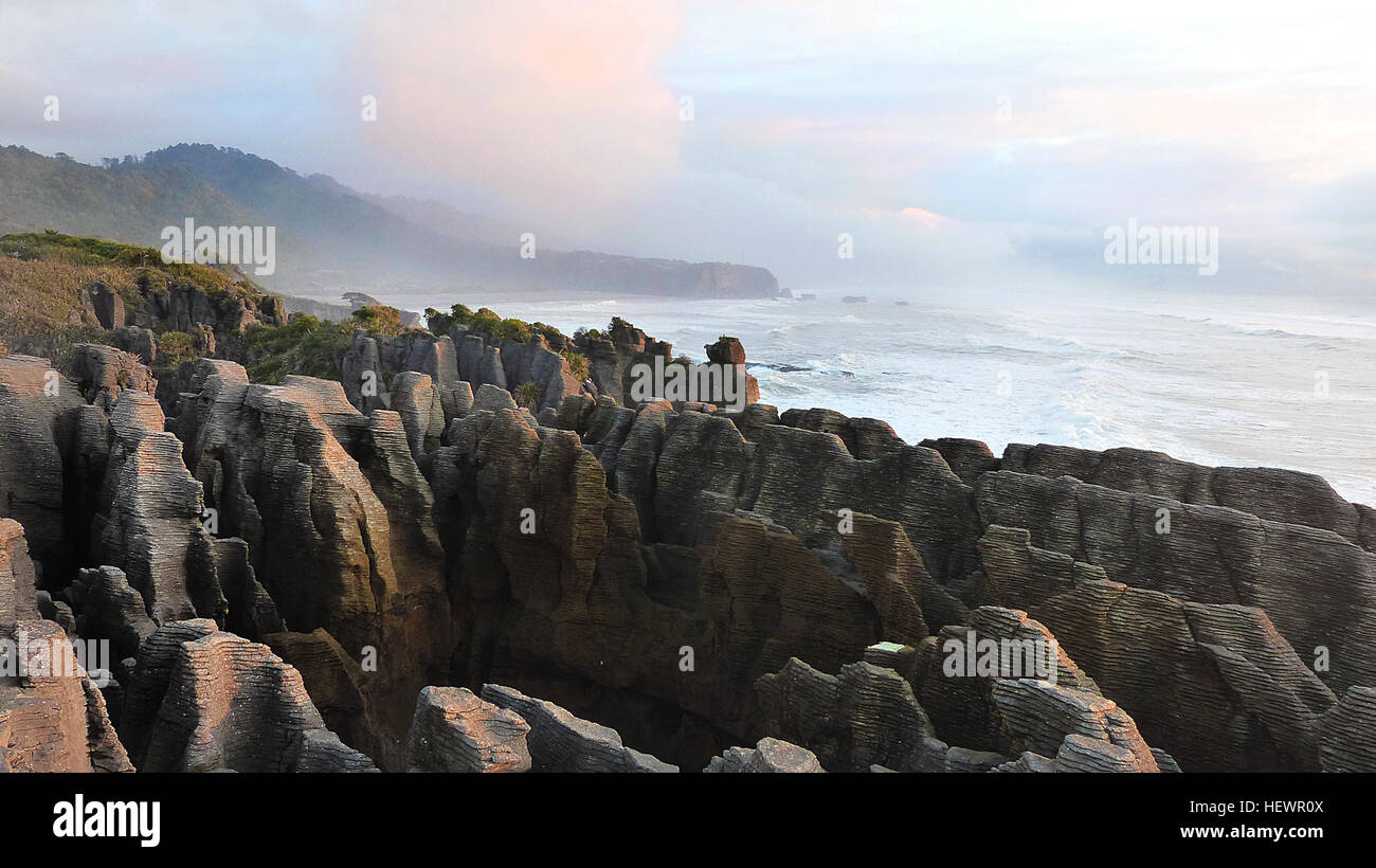 Les Pancake Rocks et Blowholes à Punakaiki sont de superbes formations calcaires formées il y a 30 millions d'années. Ces formations uniques, ressemblant à des crêpes empilées, sont mieux visibles à marée haute lorsque l'eau jaillit à travers des fleurs naturelles. Situés le long de la côte ouest de la Nouvelle-Zélande, ils offrent des vues spectaculaires et une signification géologique. Banque D'Images