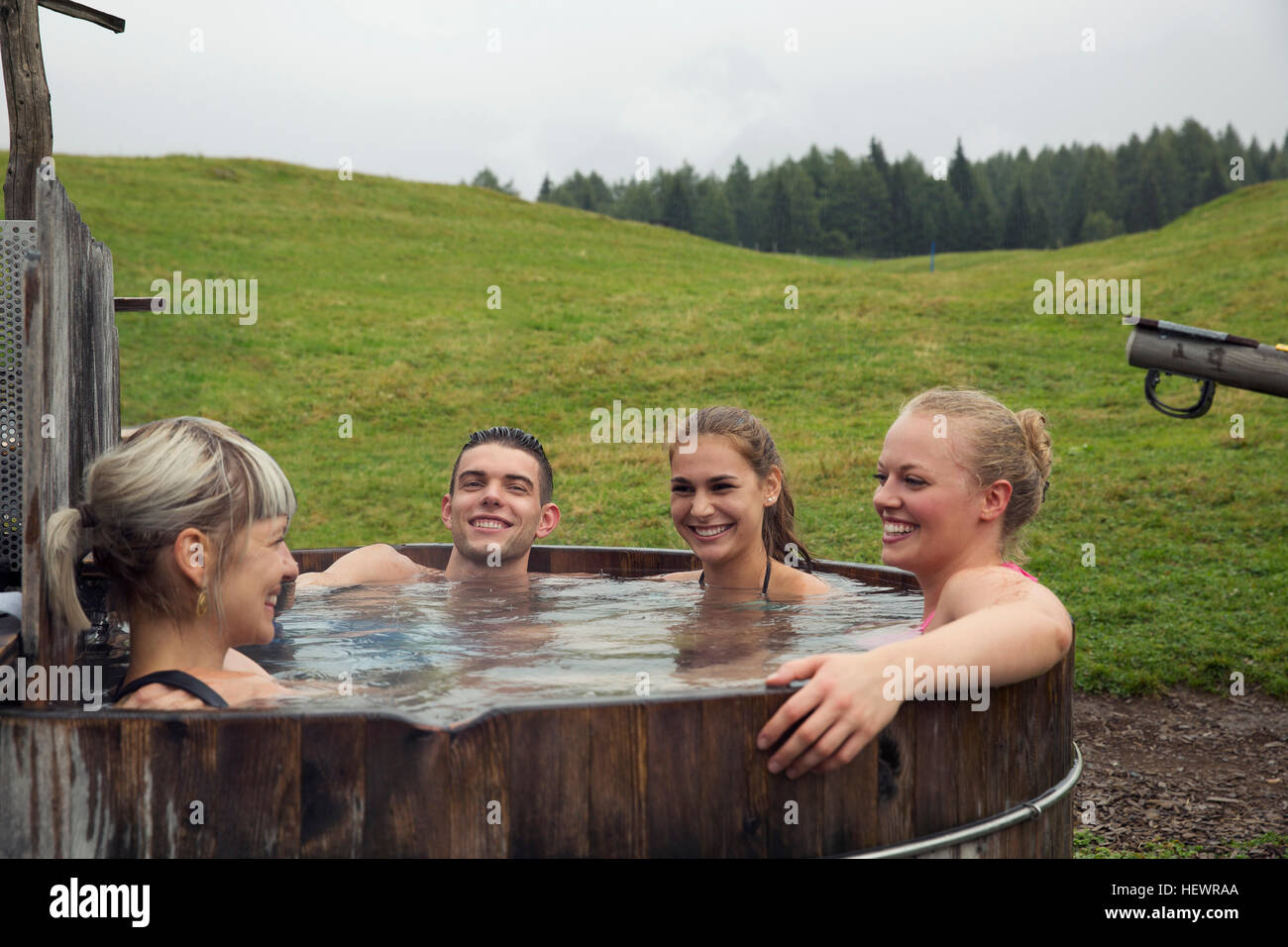 Quatre amis adultes rire tout en vous relaxant dans le bain à remous, Sattelbergalm rural, Tyrol, Autriche Banque D'Images