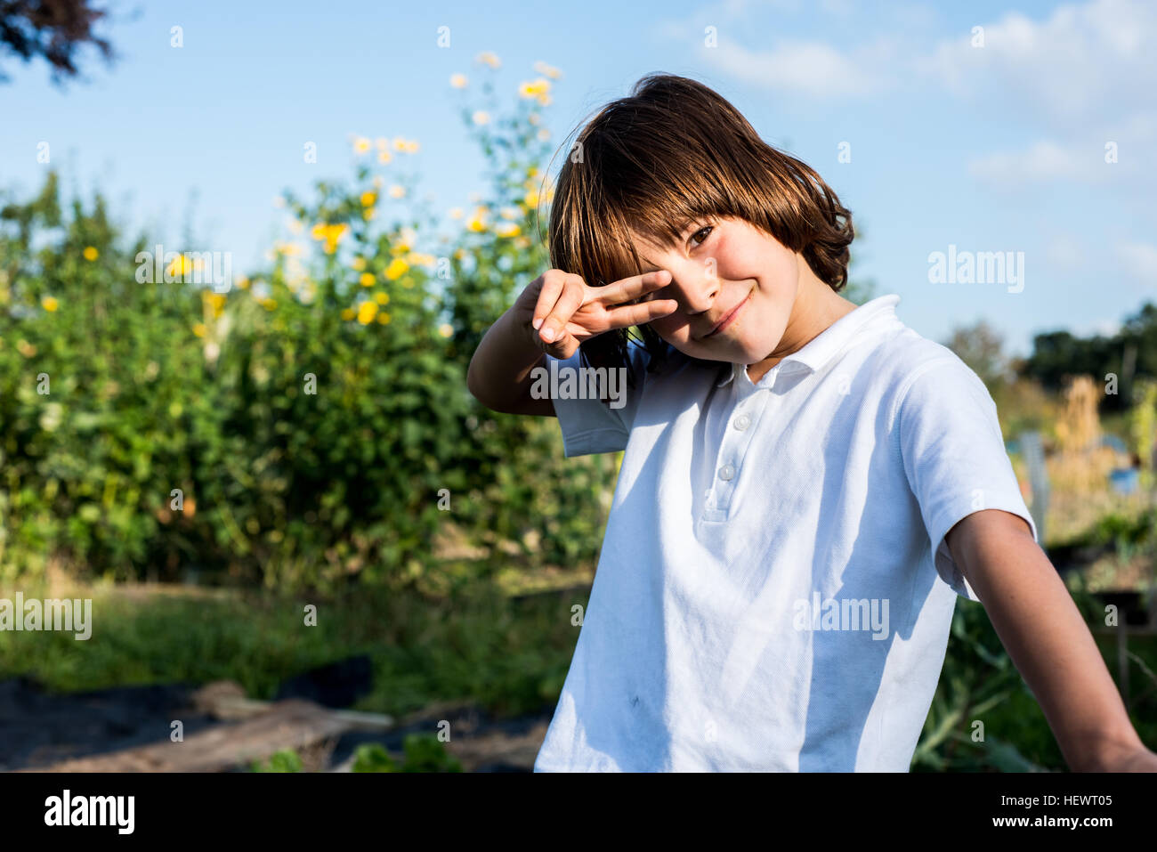 Portrait of happy boy making peace sign hand gesture dans jardin rural Banque D'Images