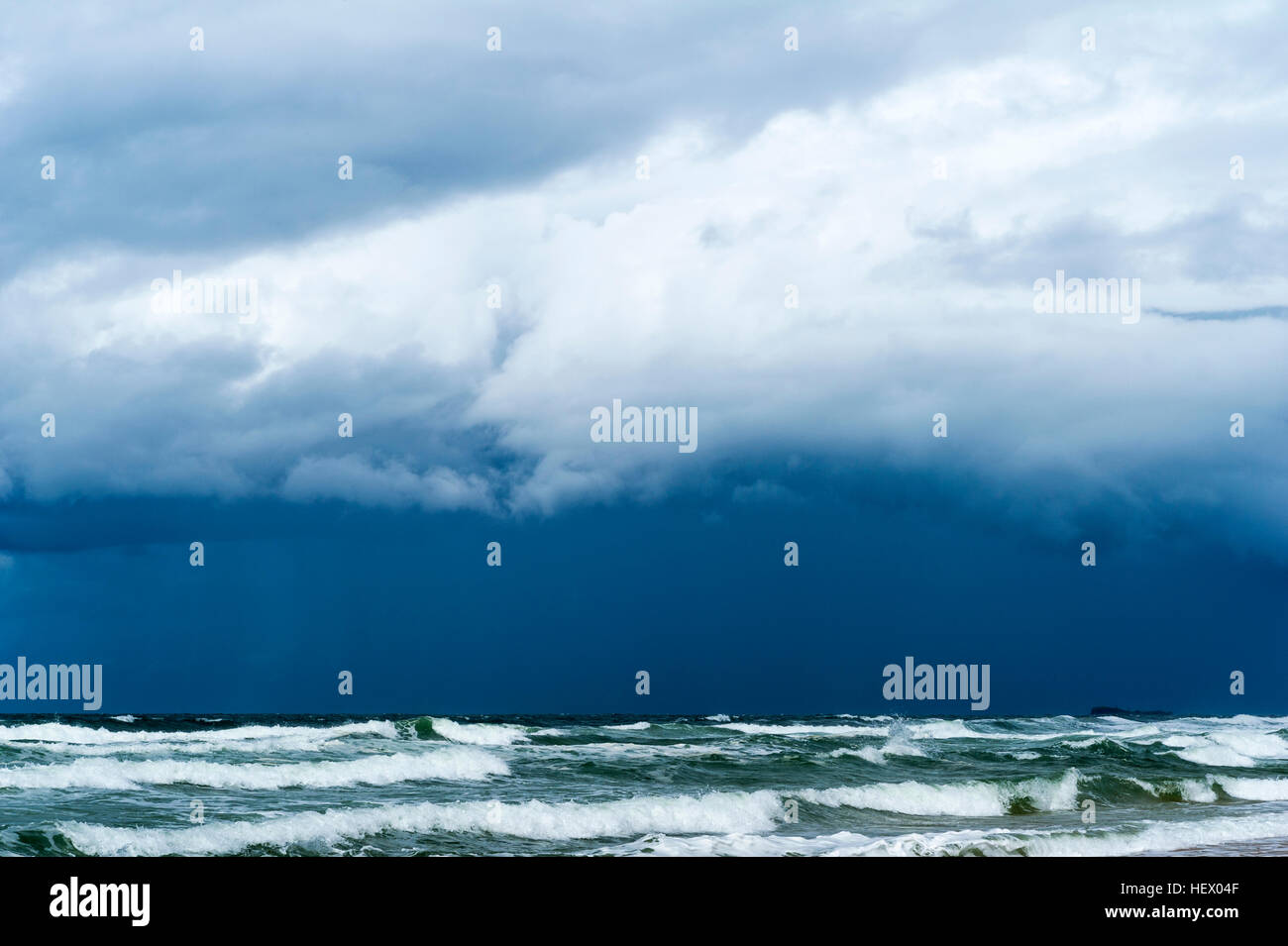 Les nuages de tempête noire inquiétante en rouleau au-dessus des vagues roulant sur une plage vide. Banque D'Images