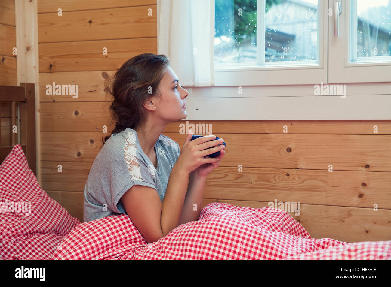 Jeune femme à la recherche d'une fenêtre de log cabin bed, Tyrol, Autriche Banque D'Images