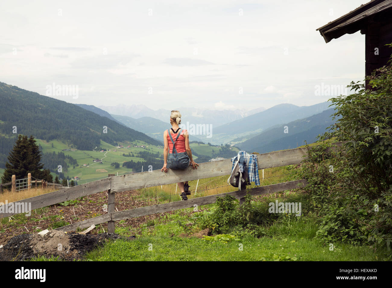 Rear view of woman sitting on fence donnant sur paysage de montagne, Sattelbergalm, Tyrol, Autriche Banque D'Images