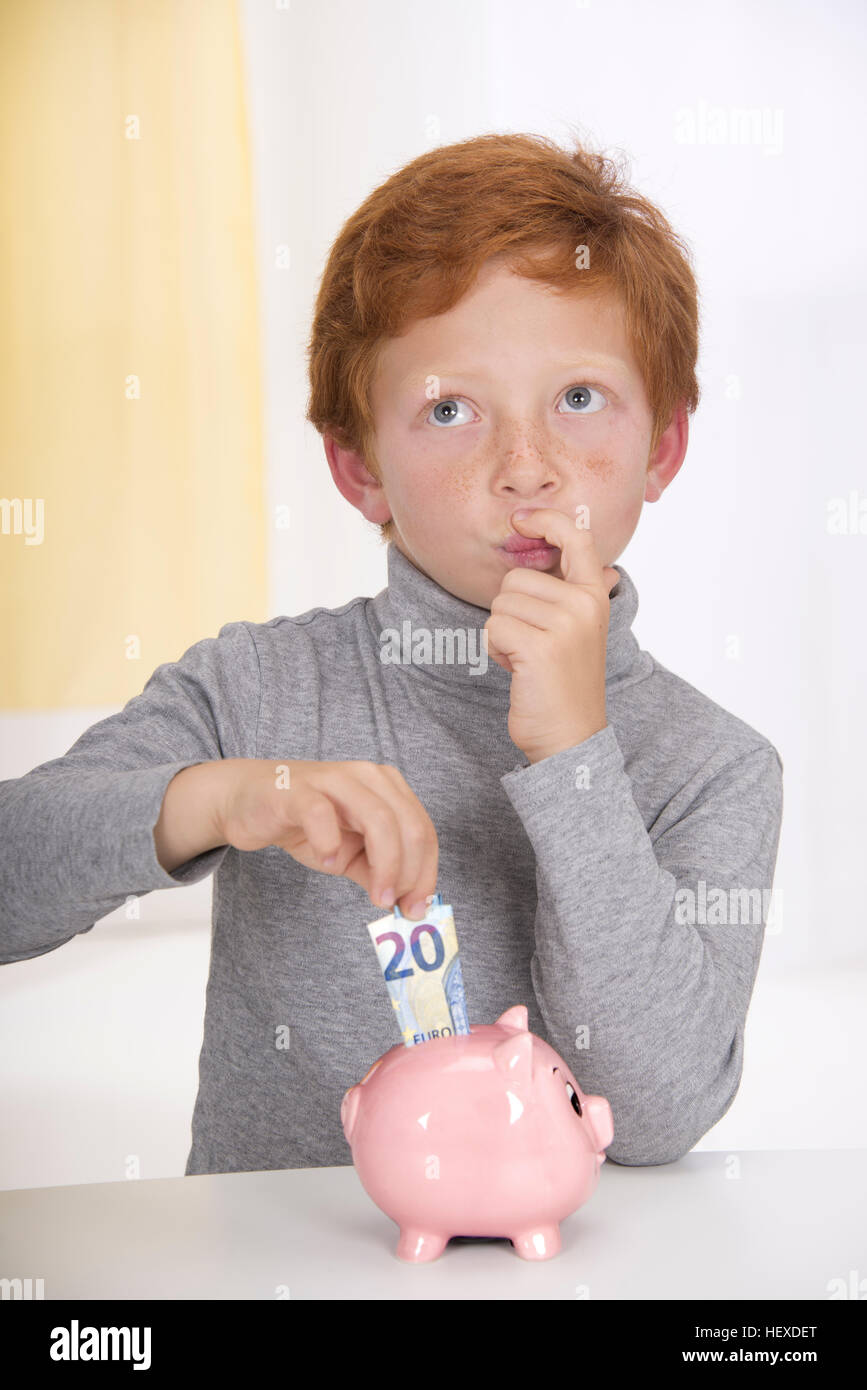 Parution du modèle. Boy putting money in piggy bank. Banque D'Images