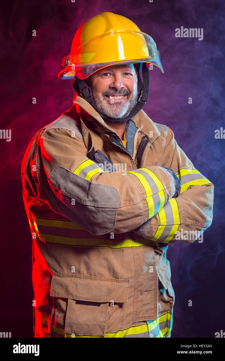 Portrait d'un pompier Pompier portant des branchements et casque. Arrière-plan est rouge et de la fumée bleue et de la lumière. Branchements sont protéger Banque D'Images