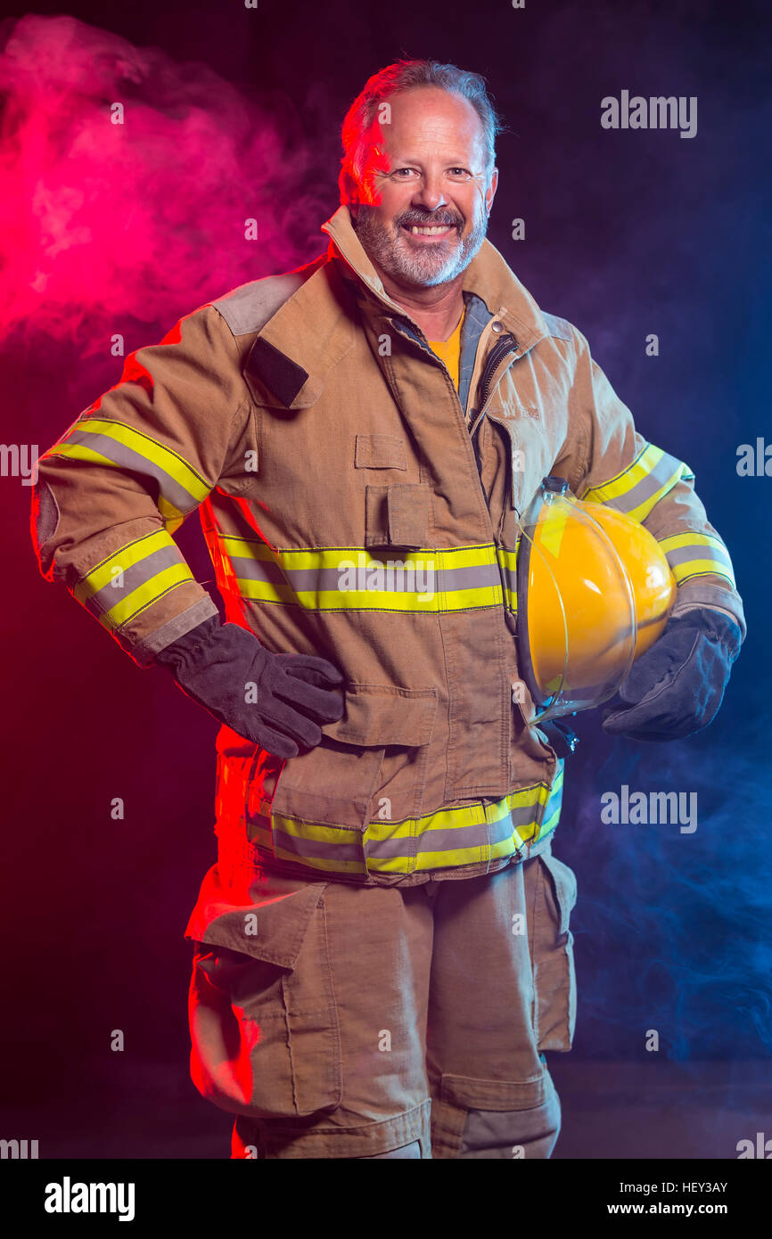 Portrait d'un pompier Pompier portant des branchements et casque. Arrière-plan est rouge et de la fumée bleue et de la lumière. Branchements sont protéger Banque D'Images