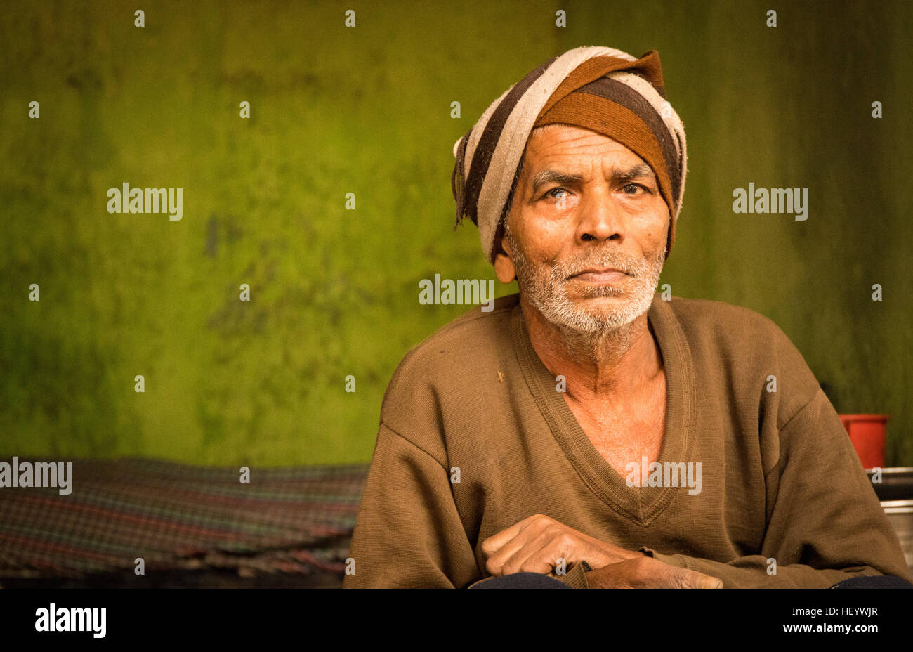 L'homme indien avec turban et brown sweater contre un fond texturé vert Banque D'Images