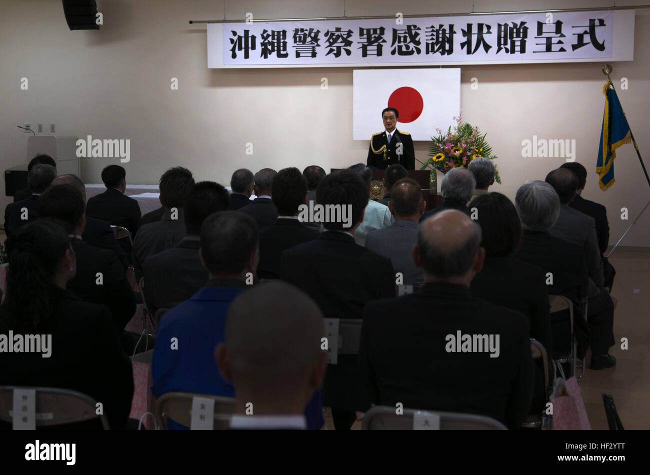 Chef de Kojun Chibana, retour centre, parle aux invités le 20 février lors d'une cérémonie de remise des prix au poste de police, la Ville d'Okinawa Prefectural Police Department, Okinawa City, Okinawa. La cérémonie a accordé les membres de l'armée américaine, les membres du personnel du ministère de la Défense américain et le Département de la Police de la ville d'Okinawa pour leurs services et d'aide à maintenir la sécurité d'Okinawa tout au long de l'année. "Vous avez montré une profonde compréhension des activités de la police et a coopéré avec la police dans la solution de divers types d'incidents et accidents en 2014," dit Chibana. "Je déclare très heureux de présenter cette le Banque D'Images