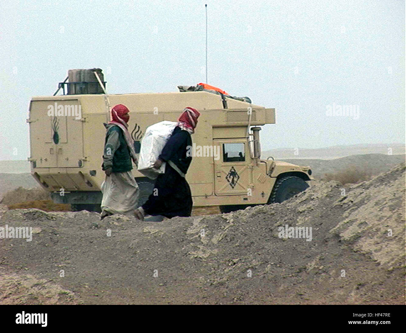 Deux civils irakiens passons un Corps des Marines des États-Unis (USMC) 5ème Marines, 1 Division de marines (MARDIV), Camp Pendleton, Californie (CA), M997 véhicule à roues multi-High-Mobility (HMMWV), partie d'un convoi qui s'est arrêté pour faire le plein au cours de l'opération IRAQI FREEDOM. (Image inférieure) ambulance HMMWV M997 l'Iraq Banque D'Images