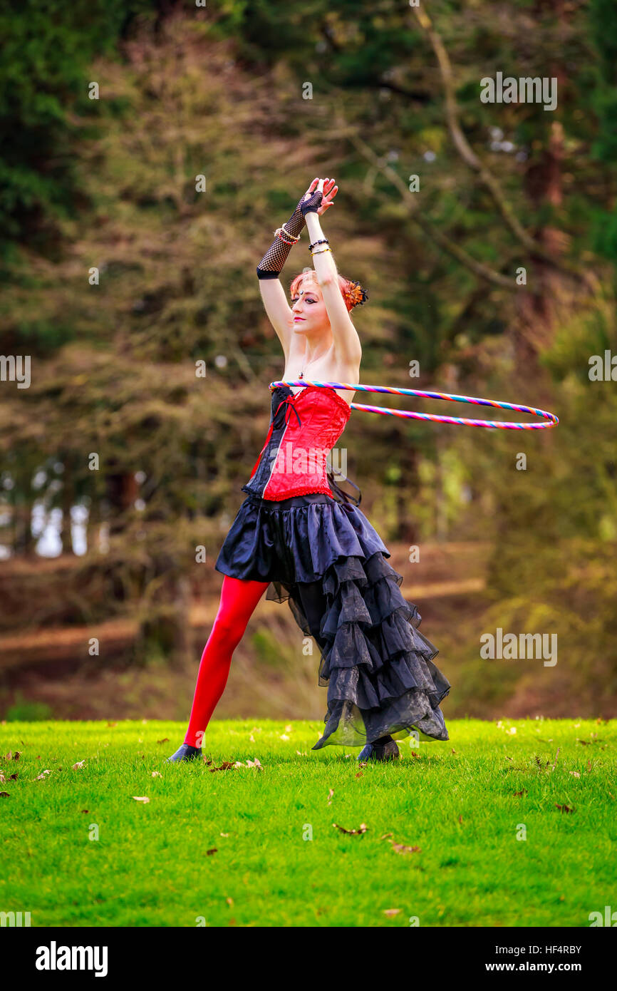 Belle jeune femme en costume de cirque jouer avec cerceau dans le parc. Banque D'Images