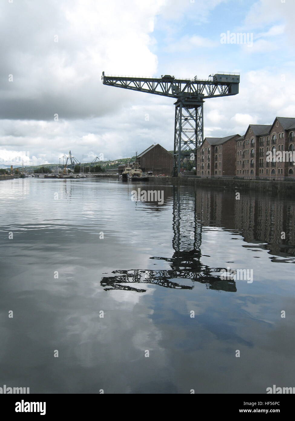Grande grue en porte-à-faux sur le port à quai reflétée dans les nuages d'eau de mer et les bateaux à ciel bleu de plus petites grues en arrière-plan Banque D'Images
