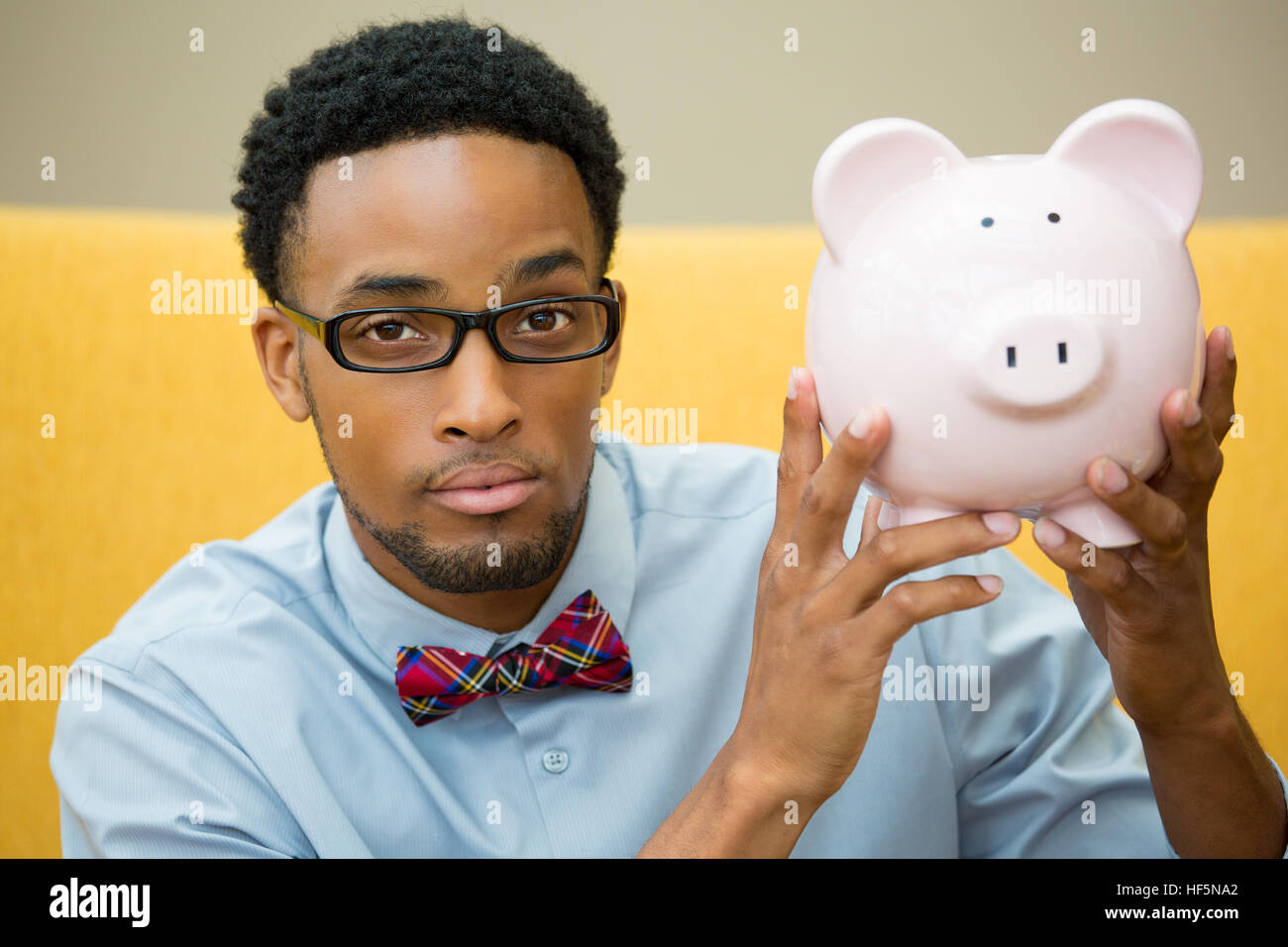 Closeup portrait of businessman heureux, en lunettes noires et bowtie, holding pink piggy bank, isolé à l'intérieur. Le budget financier Banque D'Images