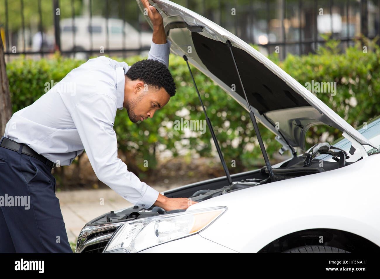 Closeup portrait, jeune homme ayant des problèmes avec sa casse auto, capot d'ouverture à essayer de réparer le moteur, Arbres verts isolés à l'extérieur de l'arrière-plan. Location ne sera pas Banque D'Images