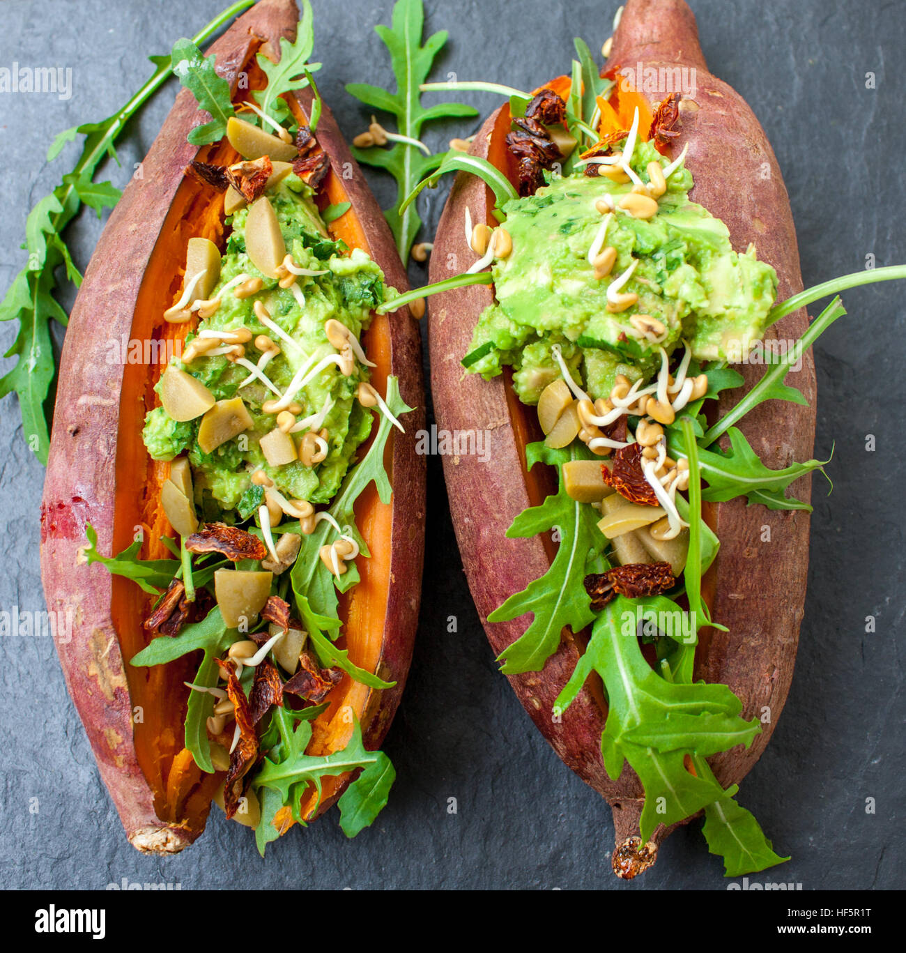 Une patate douce cuite au four farcies à la roquette, les olives, le guacamole. Vue de dessus, l'arrière-plan en ardoise. Sain Vegan le déjeuner ou le dîner. L'amour pour la santé de l'aliment cru c Banque D'Images