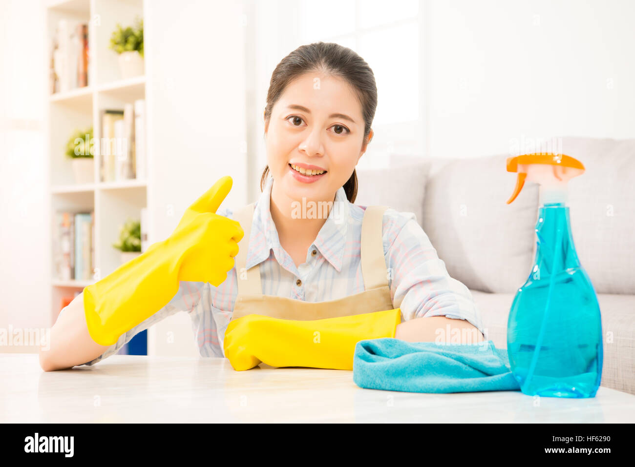 Jeune femme au foyer en gants jaunes showing Thumbs up fait le geste de nettoyage de salon à la maison. race mixte modèle chinois asiatique. Banque D'Images