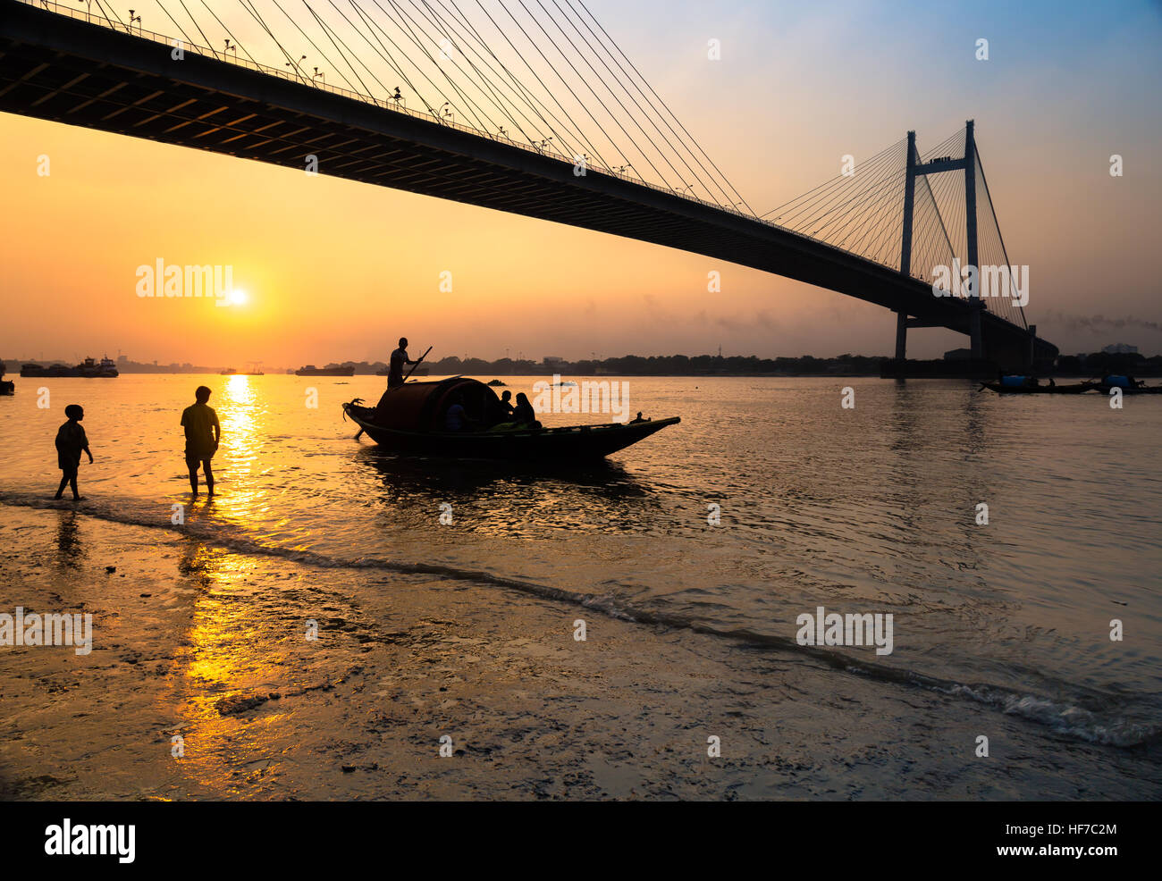 Silhouette street kids jouant au coucher du soleil sur les rives du fleuve Hooghly avec l'Vidyasagar Setu (pont) à la toile. Banque D'Images