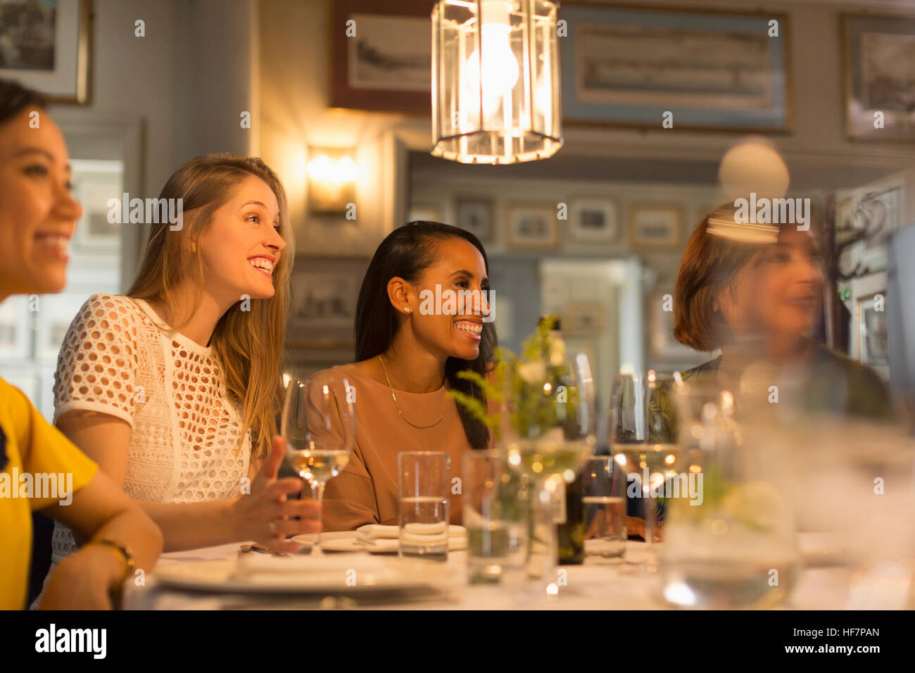 Smiling women friends à la salle à manger et à boire le vin blanc au restaurant table Banque D'Images