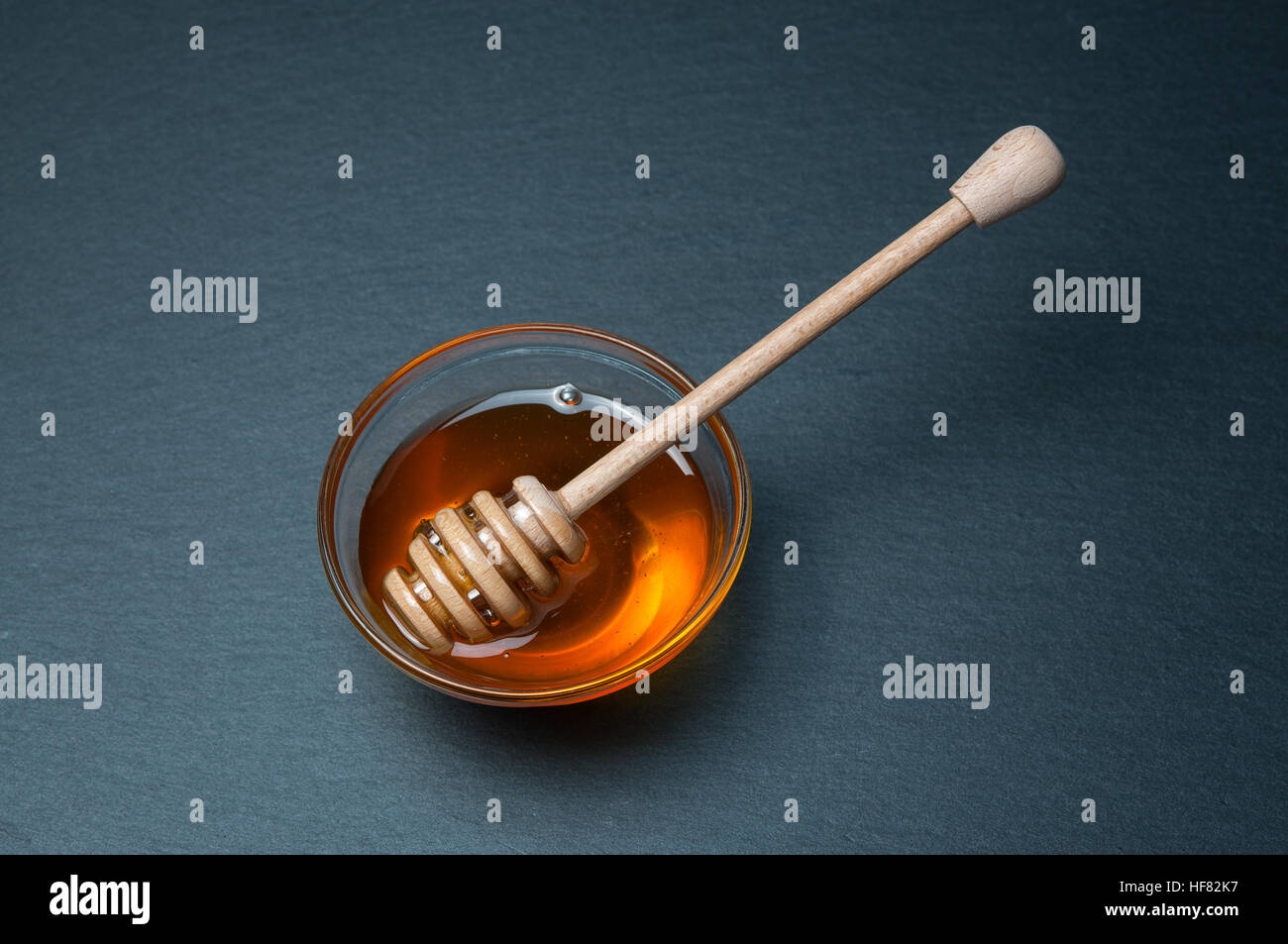 Petit bol en verre de miel naturel avec stick. Sur la table rustique en pierre noire. Banque D'Images