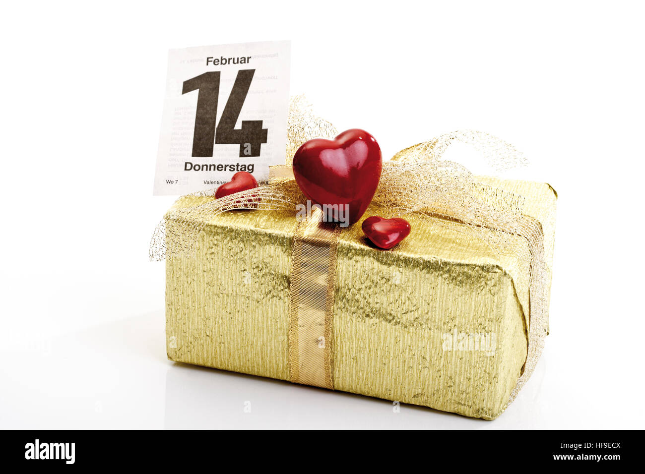 Présent enveloppé de papier cadeau et un arc d'or, calendrier La page en arrière-plan marquant le 14 février, jour de la Saint-Valentin Banque D'Images