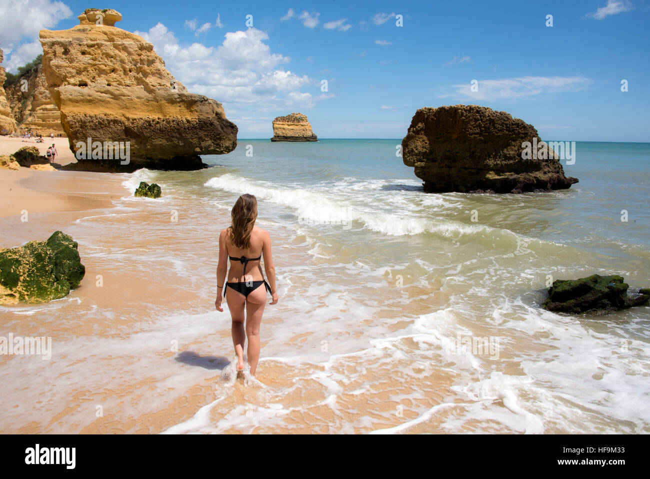 Young woman wearing bikini noir petite balade le long d'une plage de sable doré au Portugal Banque D'Images