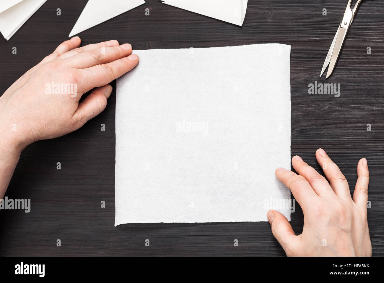 Vue du dessus des mains tenir feuille de papier avant de replier pour faire figure de table en bois brun foncé Banque D'Images