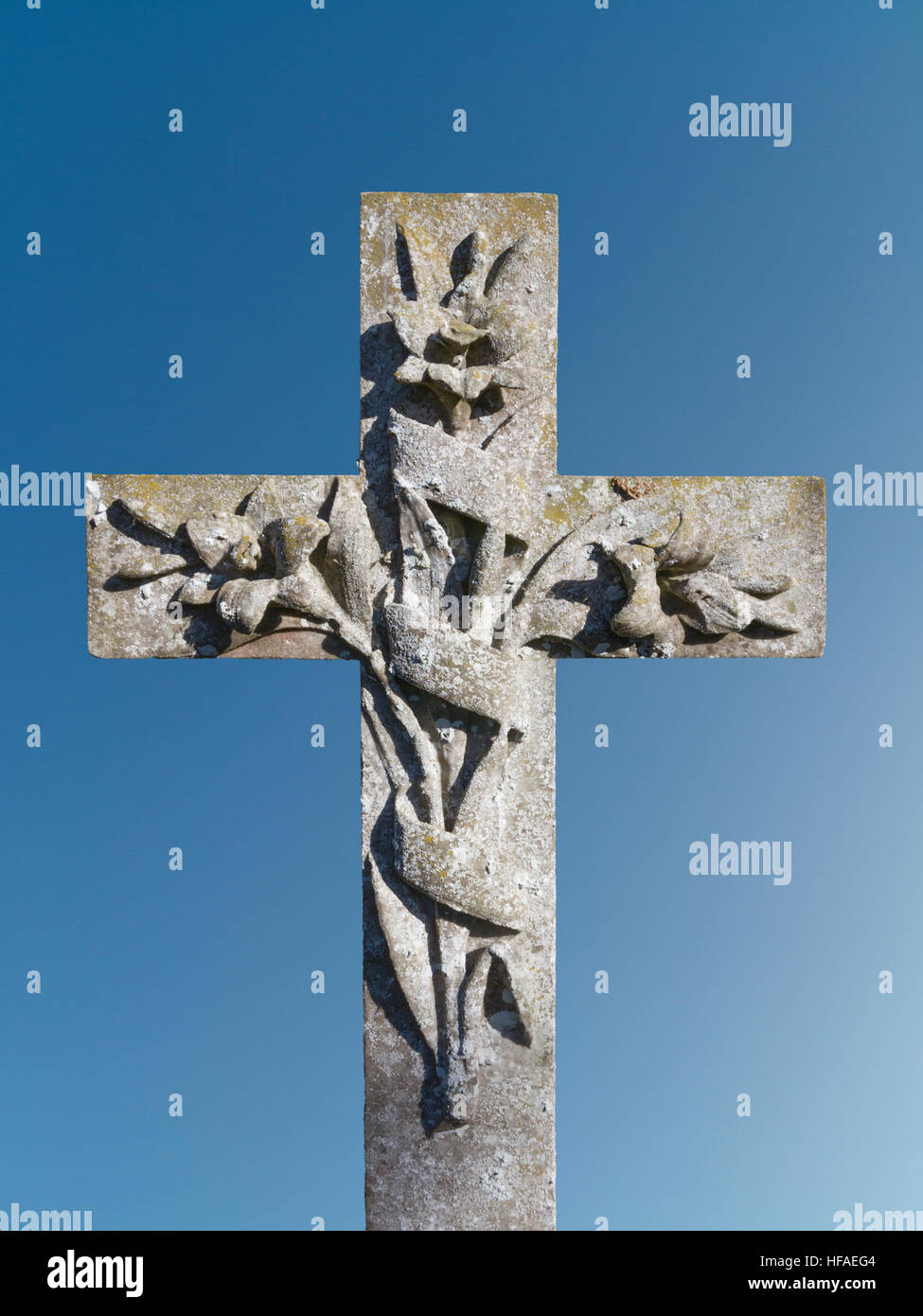 Pierre tombale croix avec lys sculpté enlacés dans une bannière contre un ciel bleu Banque D'Images