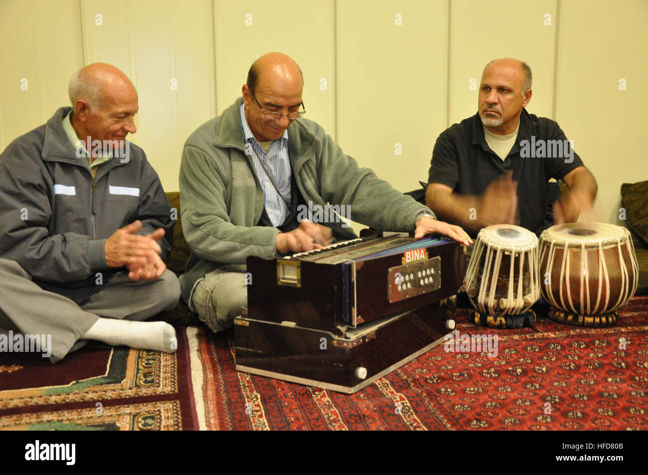Dit Shah, Ashraf Abasy et Atig Azizi exécuter 'Shawam Sadqa" au nouveau centre culturel afghan sur Camp Sapadalure en Afghanistan. La chanson est une mélodie afghane qui parle de tous les sacrifices l'un pour l'autre - une chanson d'amour. Les musiciens avaient un rendement juste avant l'inauguration du centre. Shah tape ses mains et chante, tandis que d'Abasy joue un armonium Azizi et marteaux à un rythme sur tablas. Musiciens afghans Banque D'Images