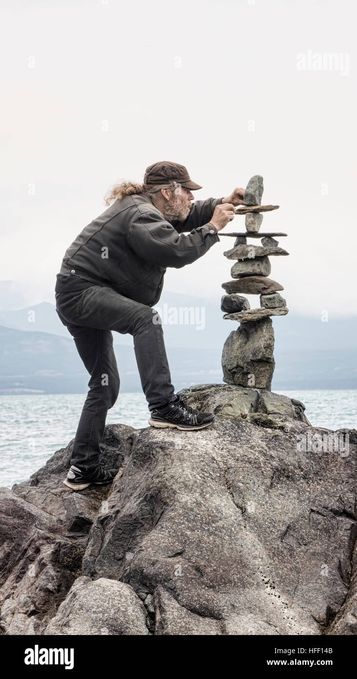 Homme d'empilage avec soin les roches dans un cairn, par la mer. Banque D'Images