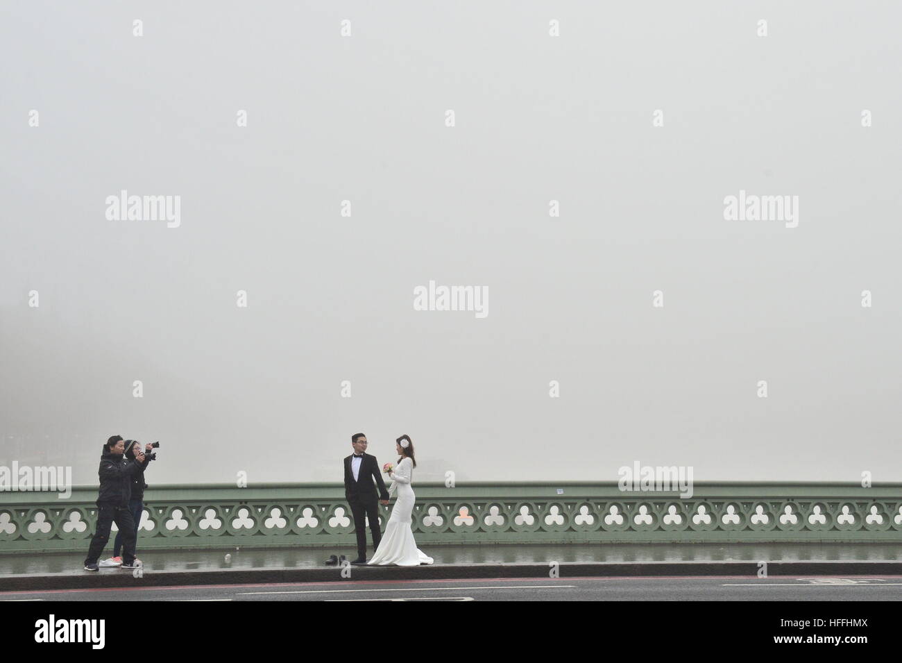 Un couple a pris des portraits de mariage de Westminster Bridge dans le brouillard dans le centre de Londres, après avoir averti les prévisionnistes de visibilité aussi bas que 100 mètres avec du brouillard et des températures sous zéro à travers de vastes étendues de l'Angleterre. Banque D'Images