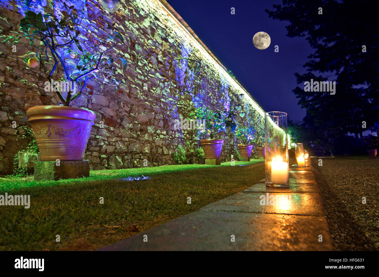Pleine lune et allumé des bougies marquer le chemin dans le jardin le long d'un mur en pierre ancienne Banque D'Images