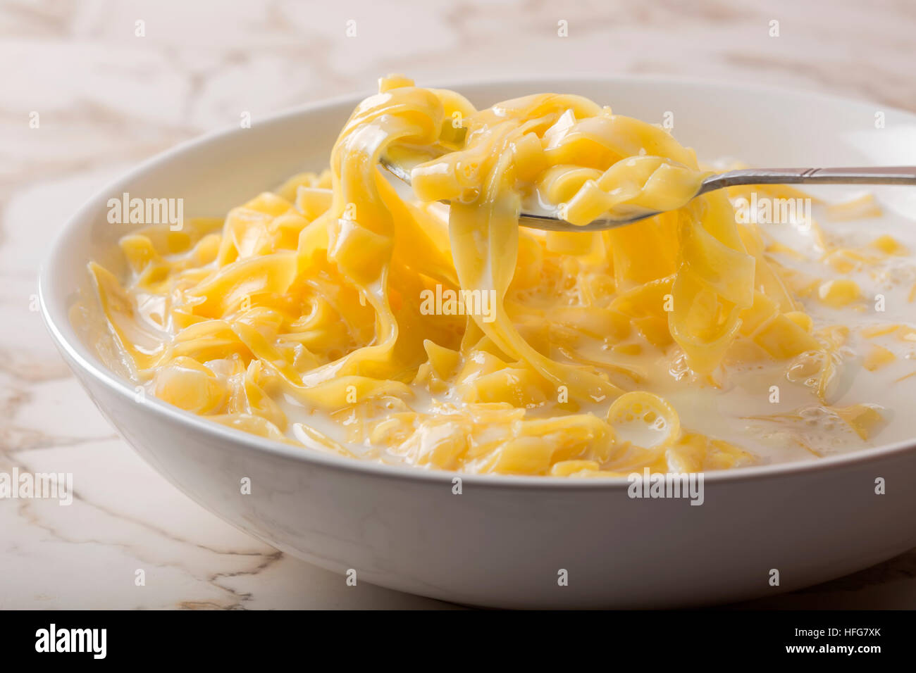 Cuillère à nouilles (tagliatelle) avec du lait et le sucre dans un bol en céramique blanche Banque D'Images