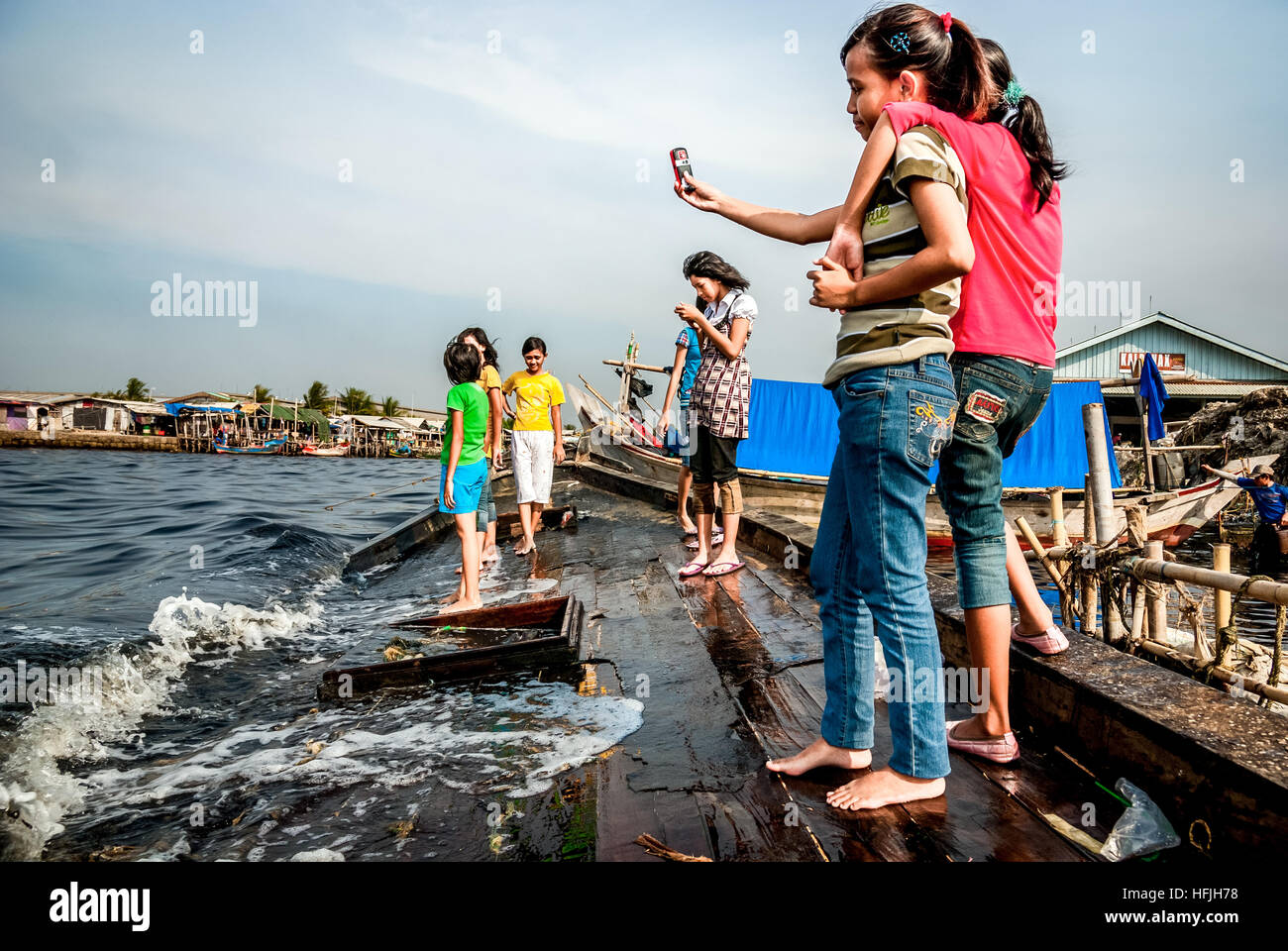 Adolescents prenant une photo selfie avec un téléphone portable sur un bateau cassé amarré à la plage dans le village de pêcheurs de Cilincing. Jakarta, Indonésie. Banque D'Images