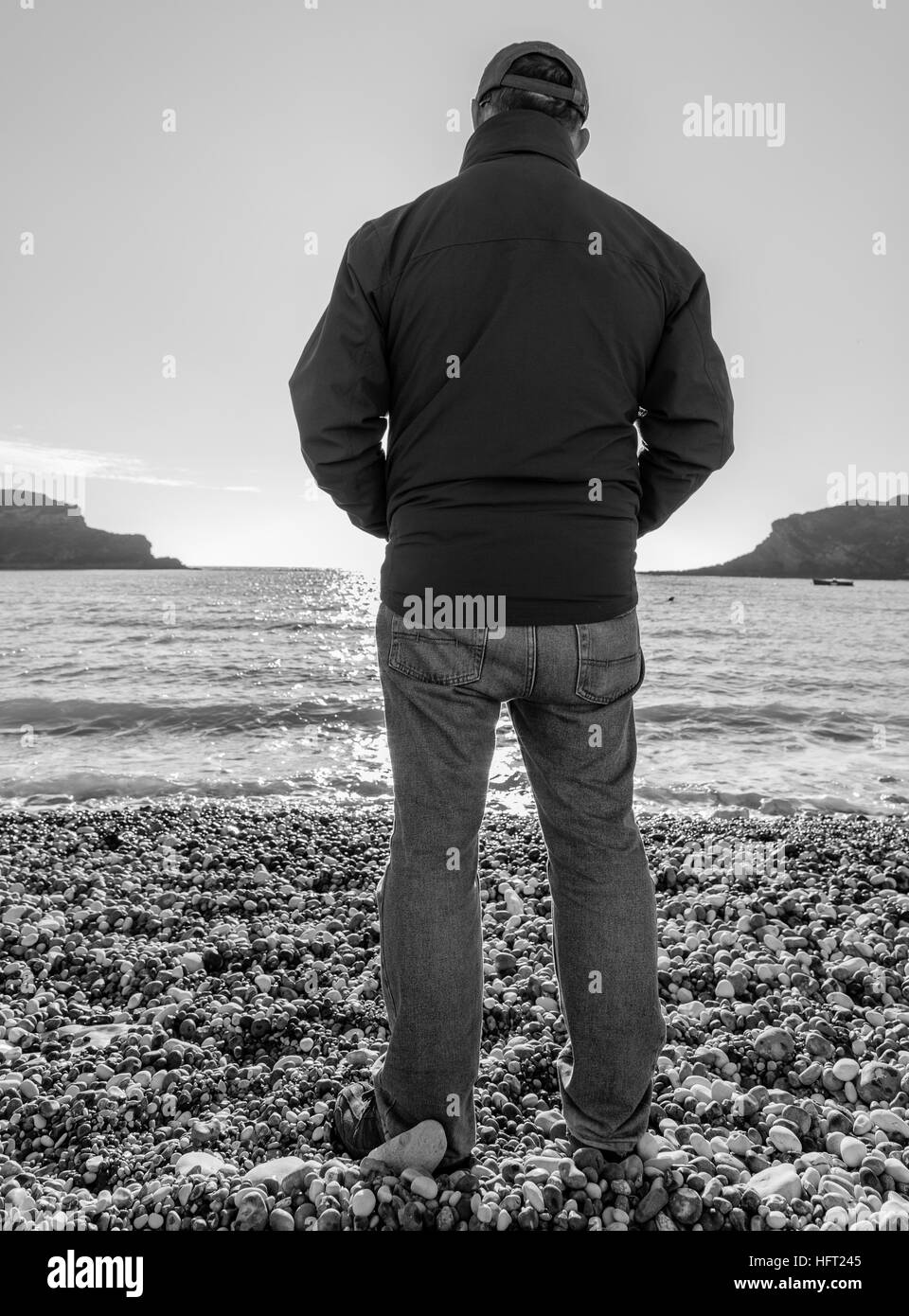 Homme debout sur une plage de galets en profitant de la vue sur une journée ensoleillée winters Banque D'Images