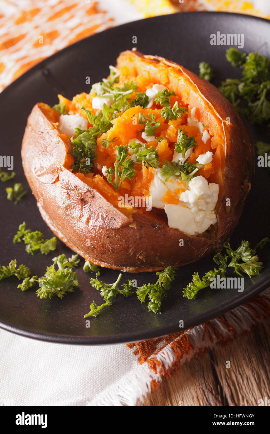 La patate douce cuite au four avec du fromage feta, les épices et le persil sur une plaque noire sur la table verticale. Banque D'Images