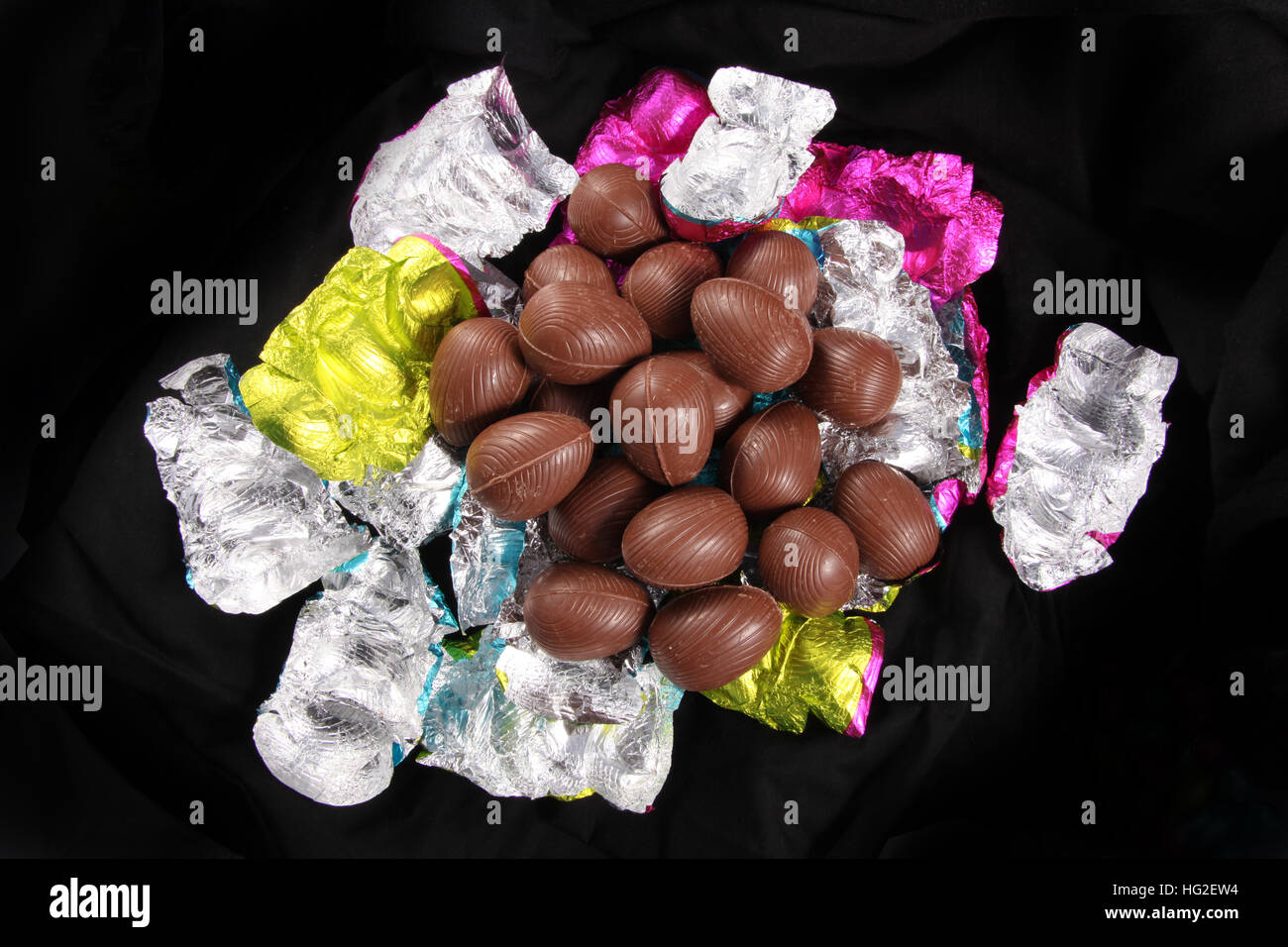 Pile d'oeufs de Pâques au chocolat décompressé de l'aluminium de couleur d'emballage d'un fond noir. Banque D'Images
