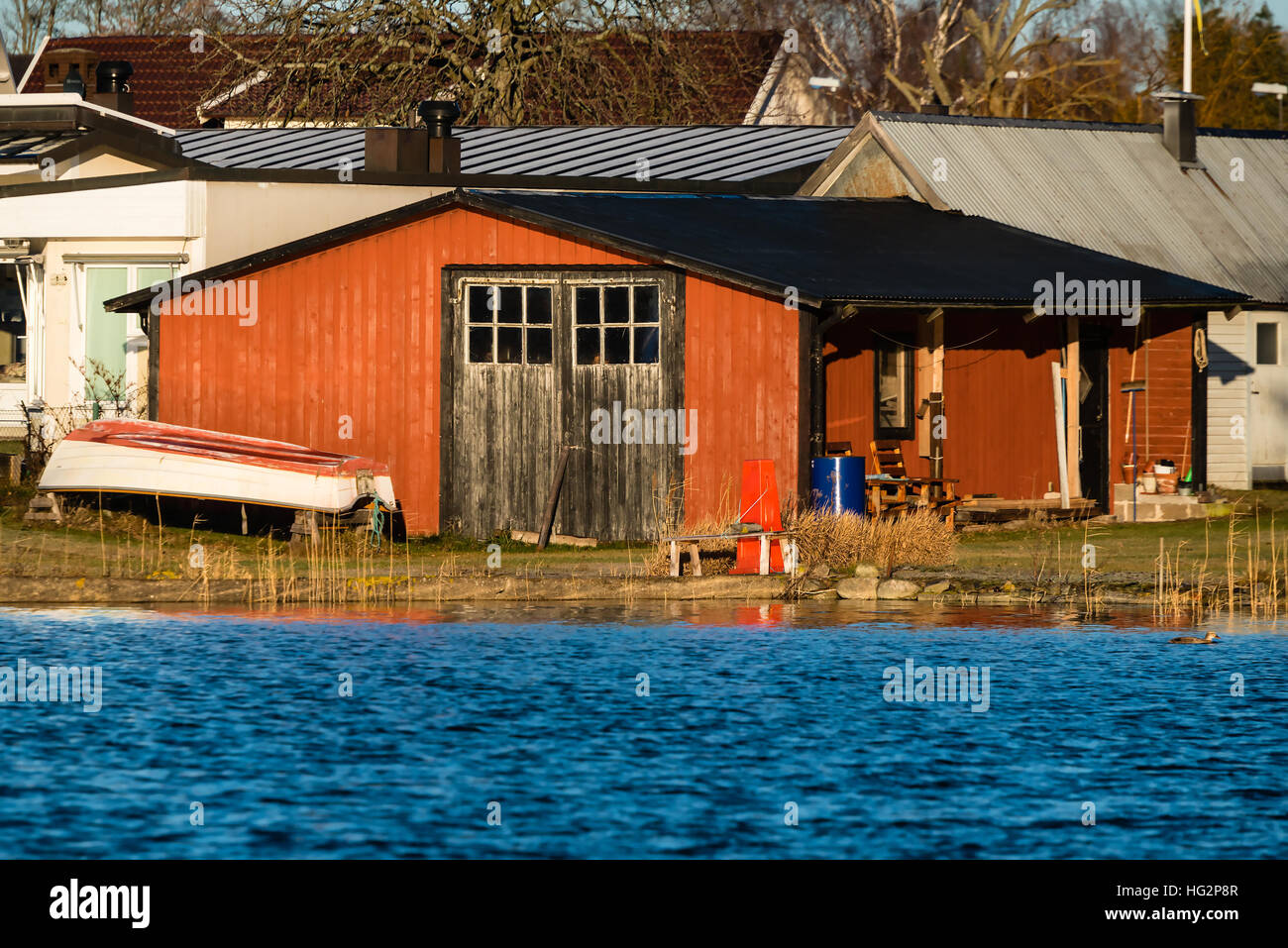 En bois rouge d'un hangar à bateaux comme vu de la mer. Les portes fermées et les petits chaloupe sur terre à l'extérieur. Calme et ensoleillé. Banque D'Images