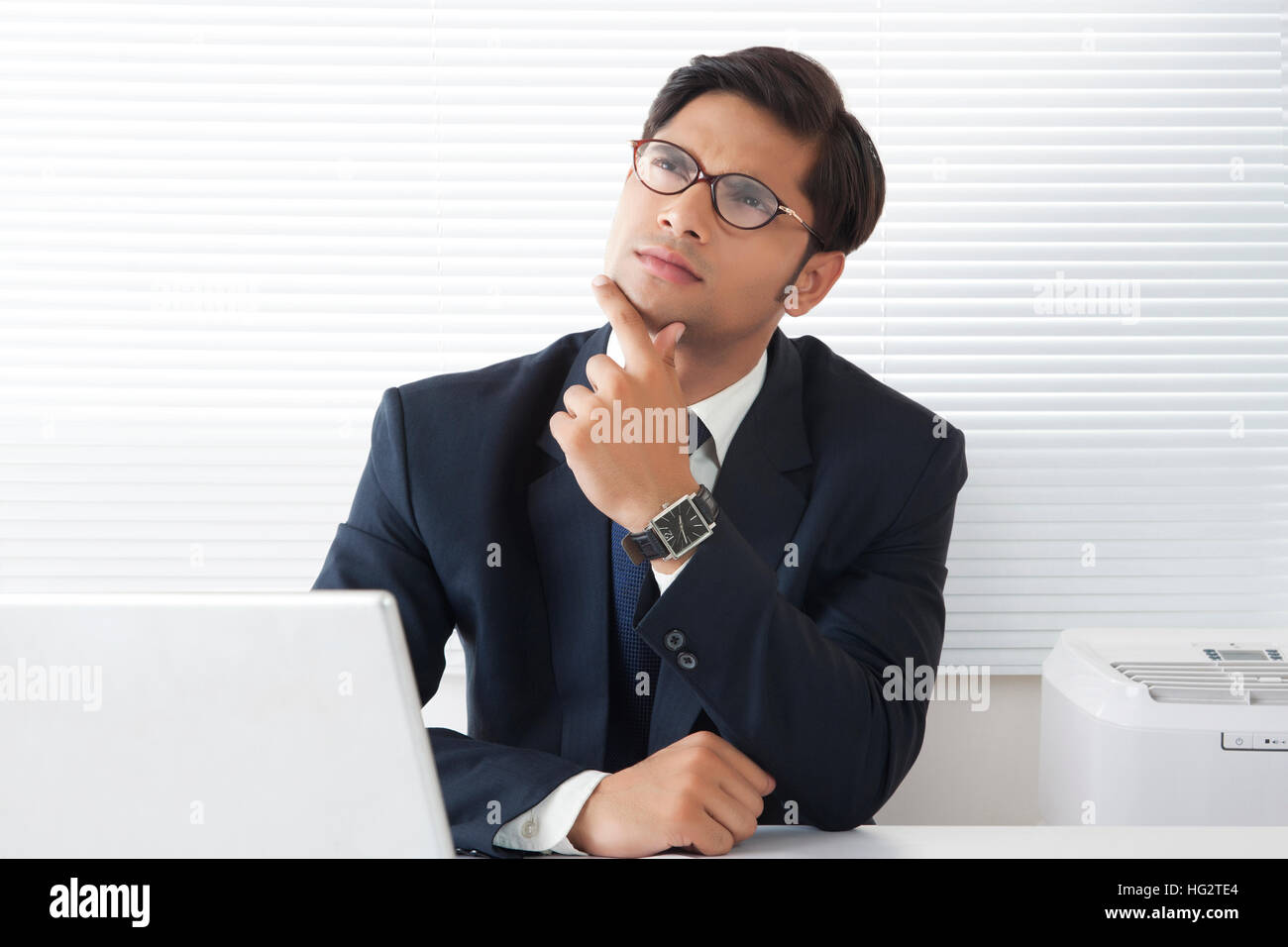 Jeune homme professionnel perdue dans ses pensées avec les doigts sur le menton et regardant vers le haut dans la cabine de bureau Banque D'Images