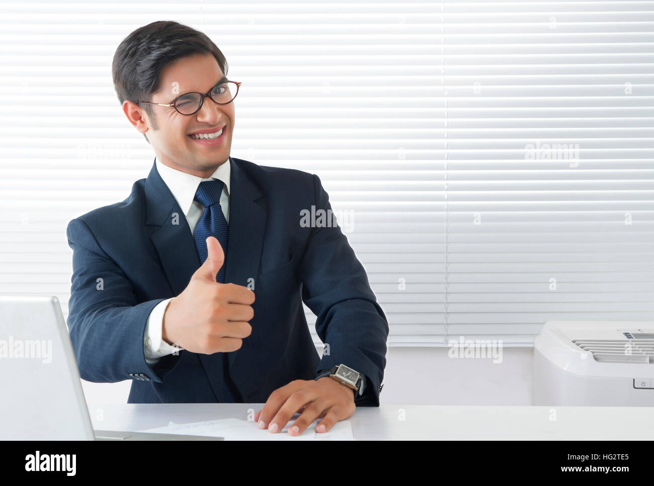 Jeune homme professionnel dans humeur heureuse showing Thumbs up sign et clignant de l'œil chez l'office de tourisme Banque D'Images
