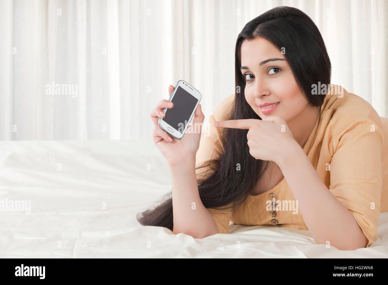 Jeune femme pointant sur téléphone mobile Banque D'Images