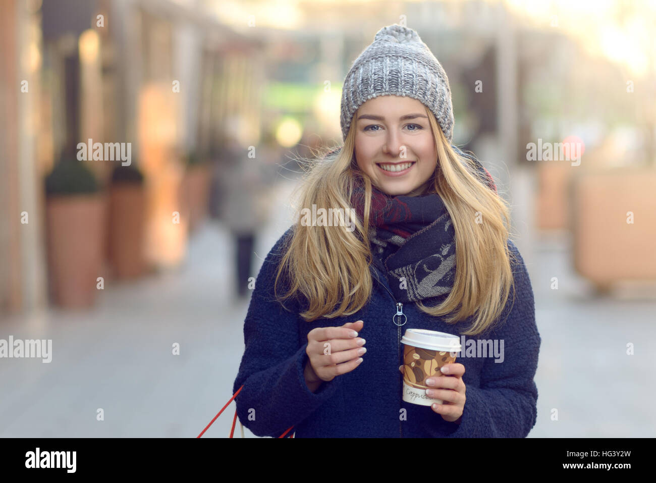 Merveilleuse jeune femme sur les achats de Noël dans un Chapeau hiver tricotés qu'il souriant derrière son regard tout en marchant dans une rue urbaine Banque D'Images