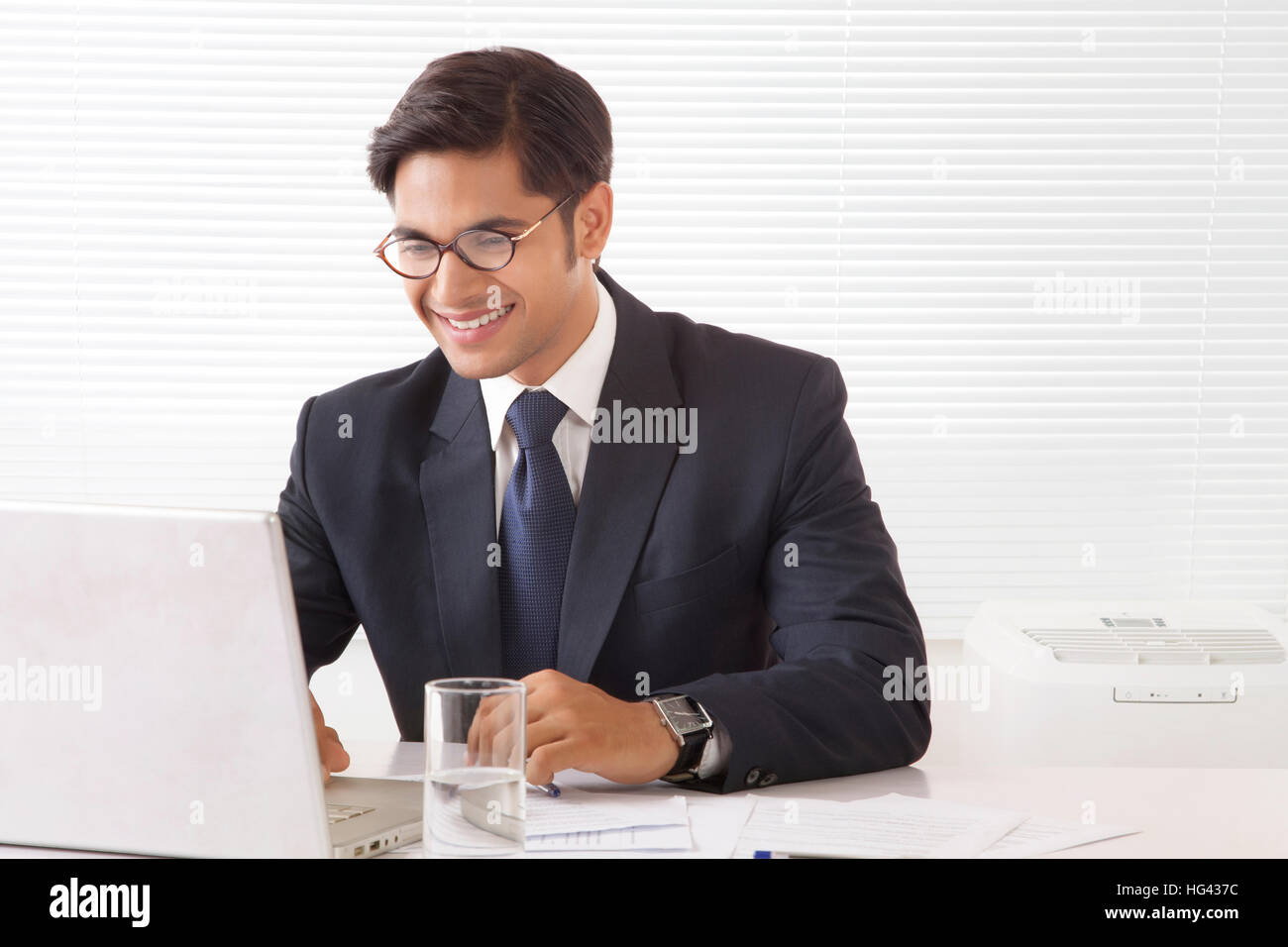 Heureux et souriant jeune homme professionnel working on laptop computer in office prix Banque D'Images