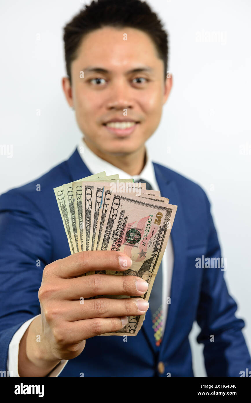 A smiling asian man in blue fonction de propagation d'argent dans la main et s'efforce d'atteindre. Expression de paiement en espèces. Traiter d'affaires officielles. Banque D'Images