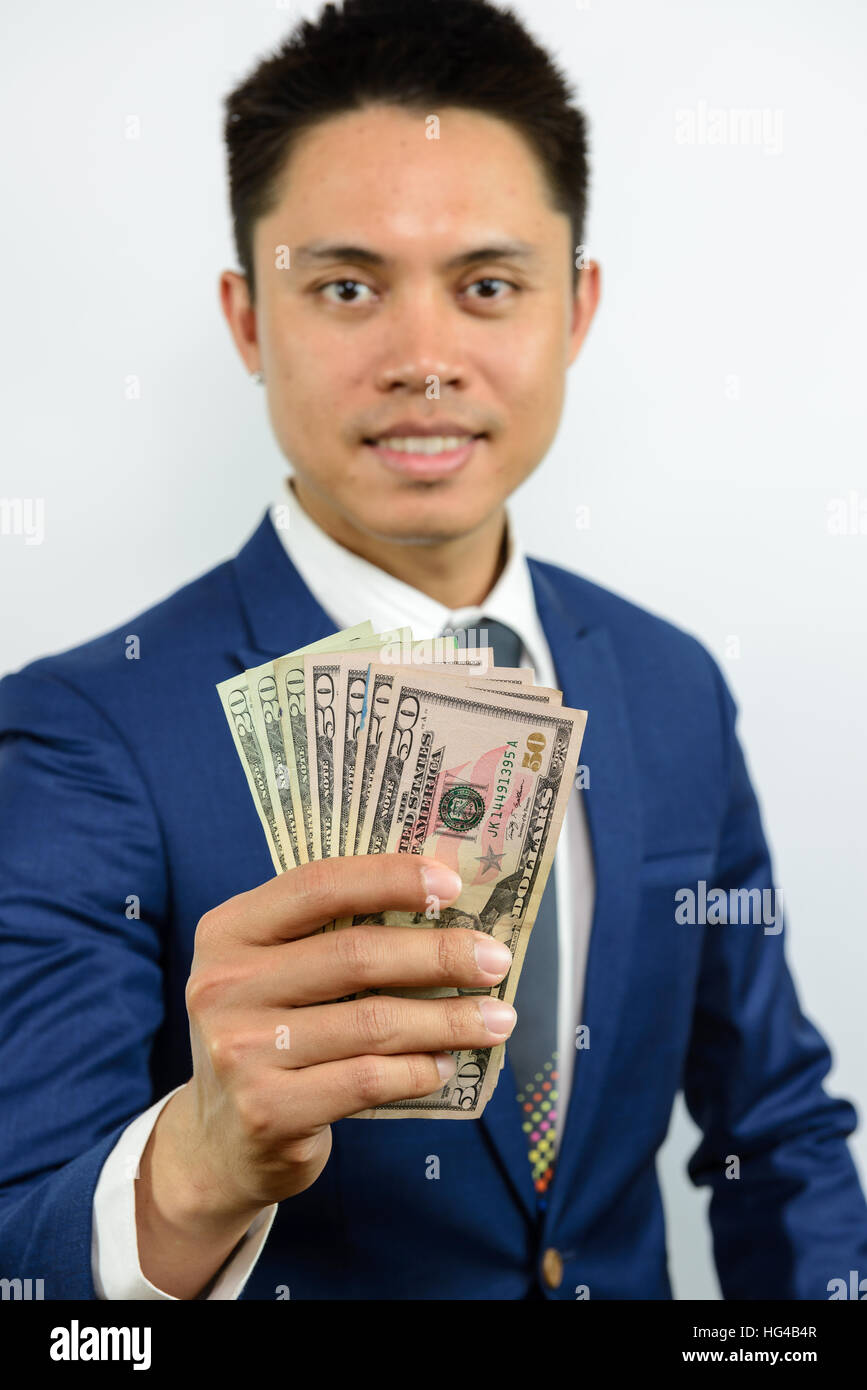 A smiling asian man in blue fonction de propagation d'argent dans la main et s'efforce d'atteindre. Expression de paiement en espèces. Traiter d'affaires officielles. Banque D'Images