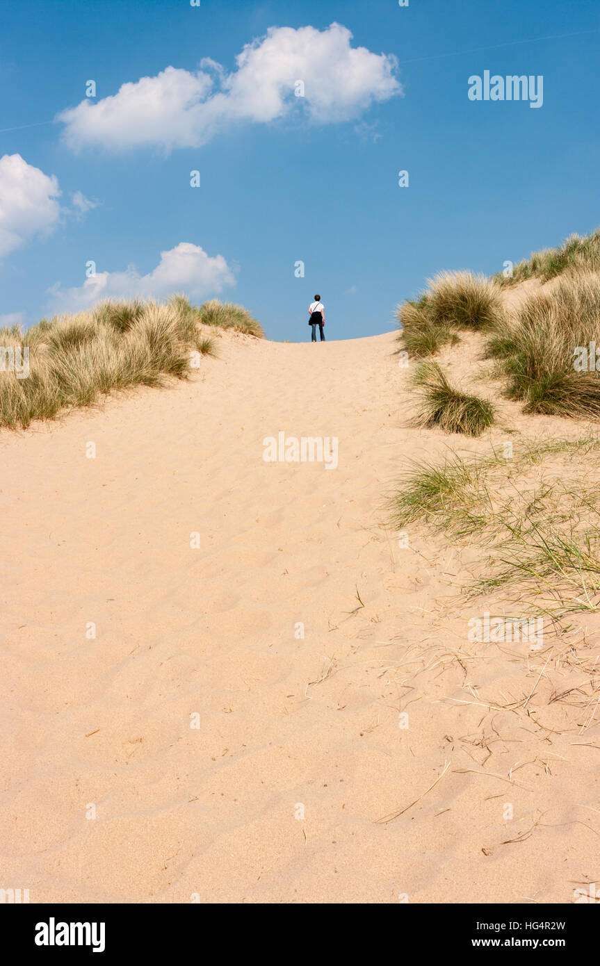 Jeune femme debout au sommet d'une dune de sable au soleil du printemps, à Burnham Overy Staithe, Norfolk, Angleterre, Royaume-Uni. Banque D'Images
