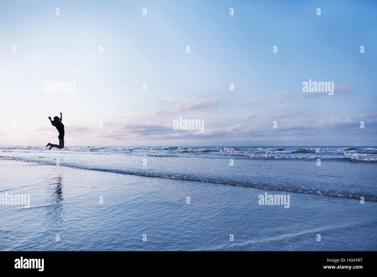 Femme sautant de joie sur la plage au lever du soleil Banque D'Images