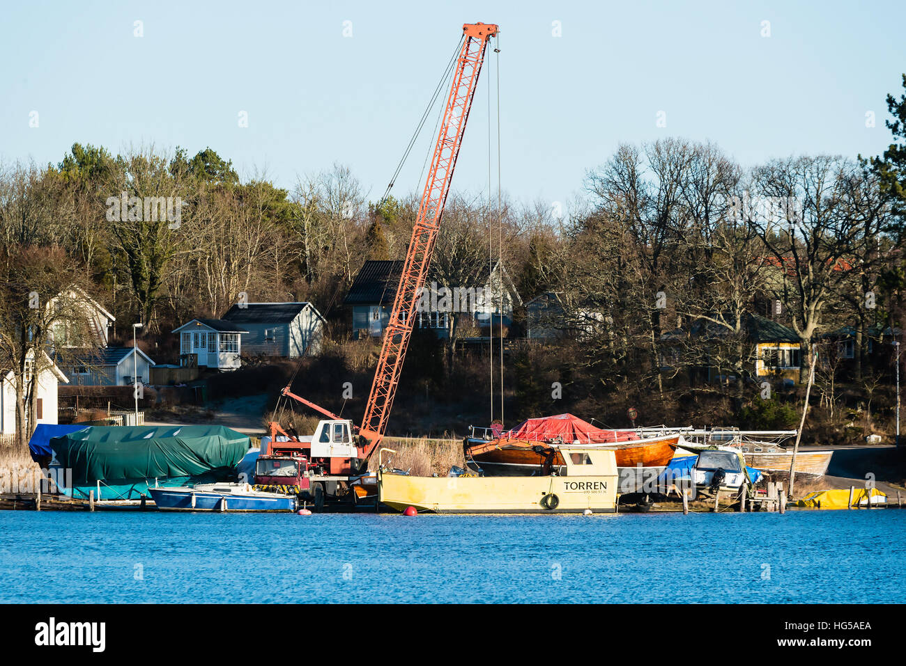 Ronneby, Suède - 2 janvier 2017 : documentaire de style balnéaire. Une grue mobile et quelques bateaux dans la marina. Maisons dans la forêt en arrière-plan. Banque D'Images