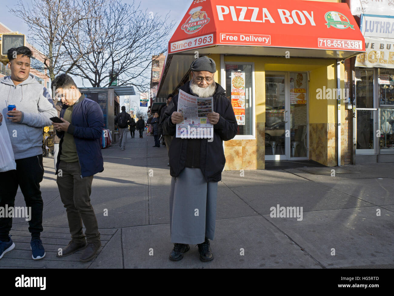 Un homme avec une barbe lisant un journal en bengali sur la 37e Rue à Jackson Heights, Queens, New York. Banque D'Images