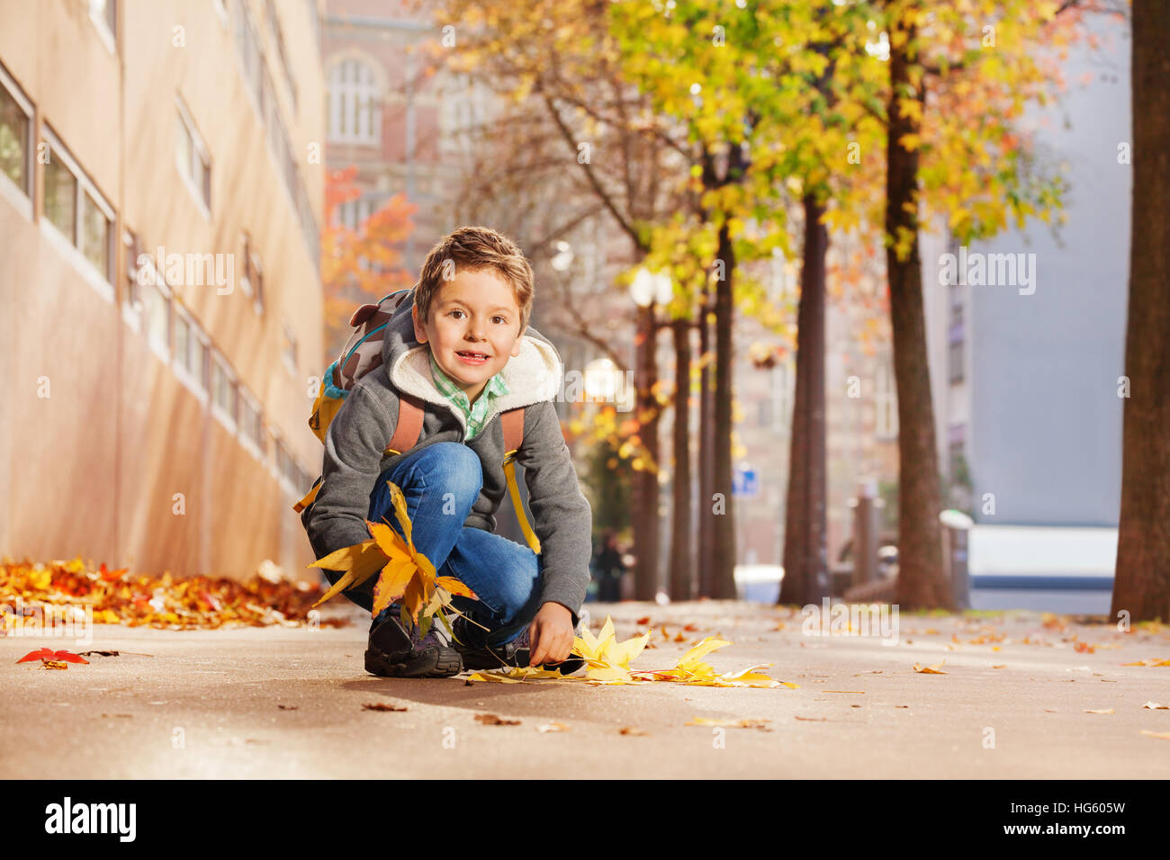 Cute boy la collecte des feuilles d'érable sur le chemin de sa maison Banque D'Images