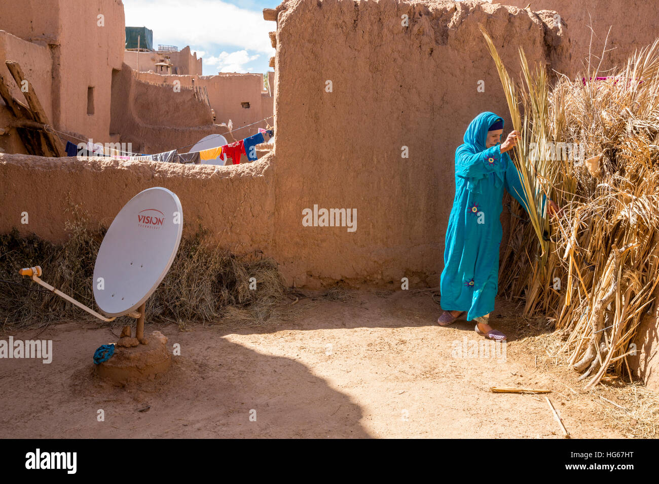 Ksar Elkhorbat, Maroc. Femme berbère Amazigh Sélection Palmier à brûler pendant la cuisson du pain, sur les toits de la Casbah avec antenne satellite. Banque D'Images