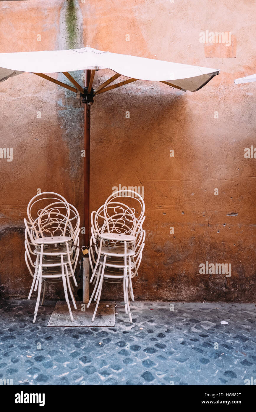 Un parasol et des chaises métalliques empilés à l'extérieur d'un restaurant dans la zone Trastevere de Rome, Italie. Banque D'Images