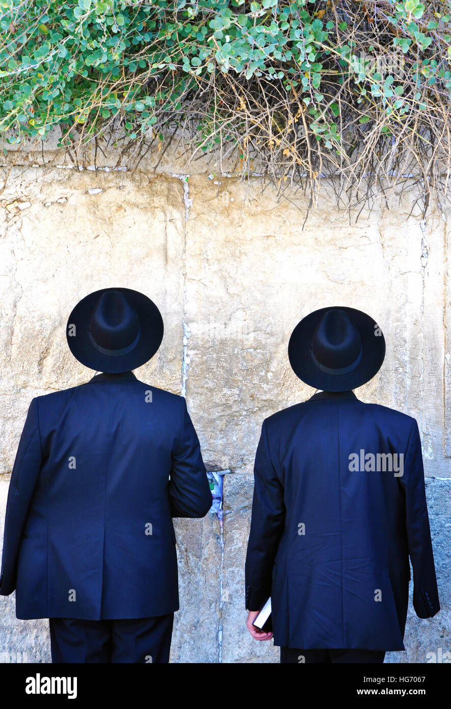 Deux hommes juifs portant des costumes noirs et des chapeaux, priant au mur occidental à Jérusalem Banque D'Images